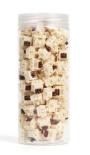 A clear cylindrical plastic jar filled with cream-colored mechanical keyboard switches, photographed against a plain white background.